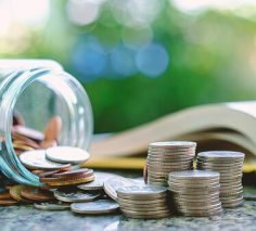 Pile of money coins in and outside the glass jar on blurred book and natural green background for financial and education concept